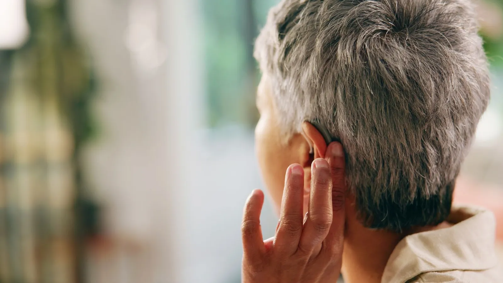 Close-up of a person wearing a modern behind-the-ear hearing aid, touching it gently with their fingers
